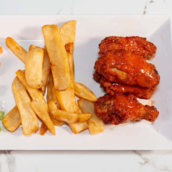 A white rectangular plate holds golden french fries and several red, saucy chicken wings.