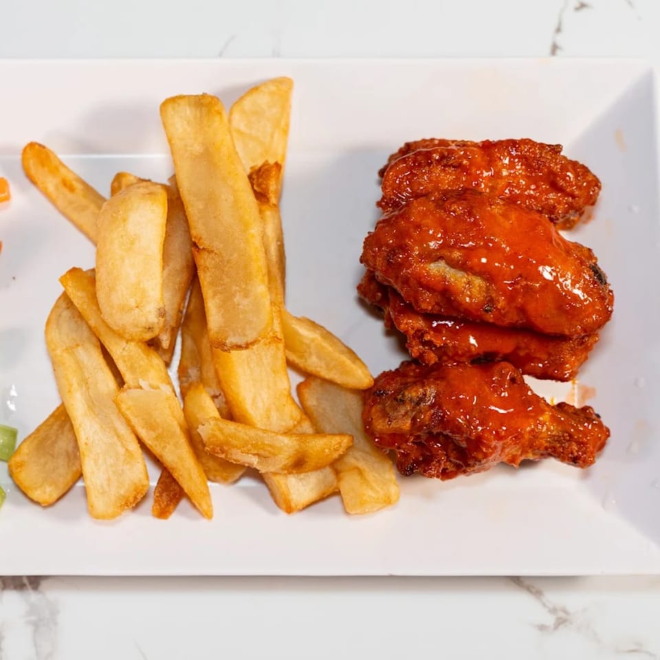A white rectangular plate holds golden french fries and several red, saucy chicken wings.