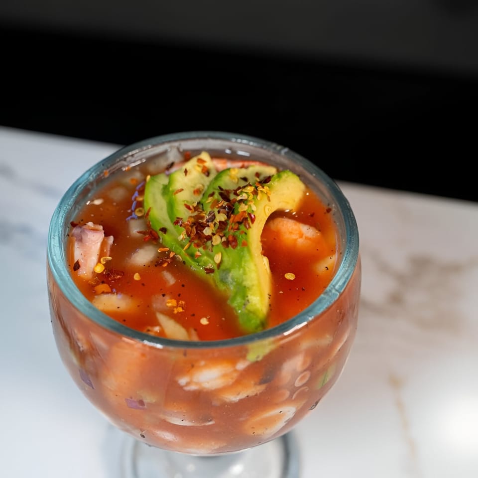 Mexican shrimp cocktail with avocado slices and chili flakes in a glass.