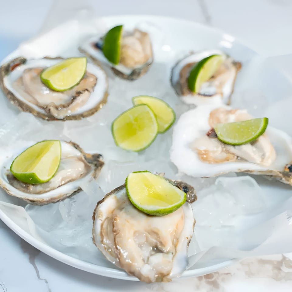 Six fresh oysters on the half shell with lime wedges, served on a bed of ice.